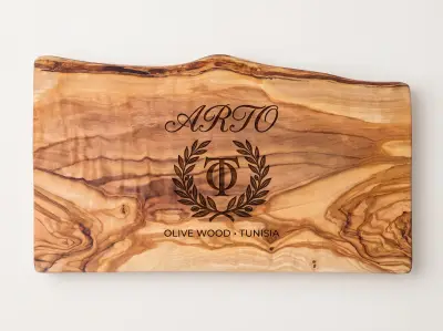 The same live-edge olive wood board after laser engraving, carrying a customer wordmark, a laurel emblem and an OLIVE WOOD line